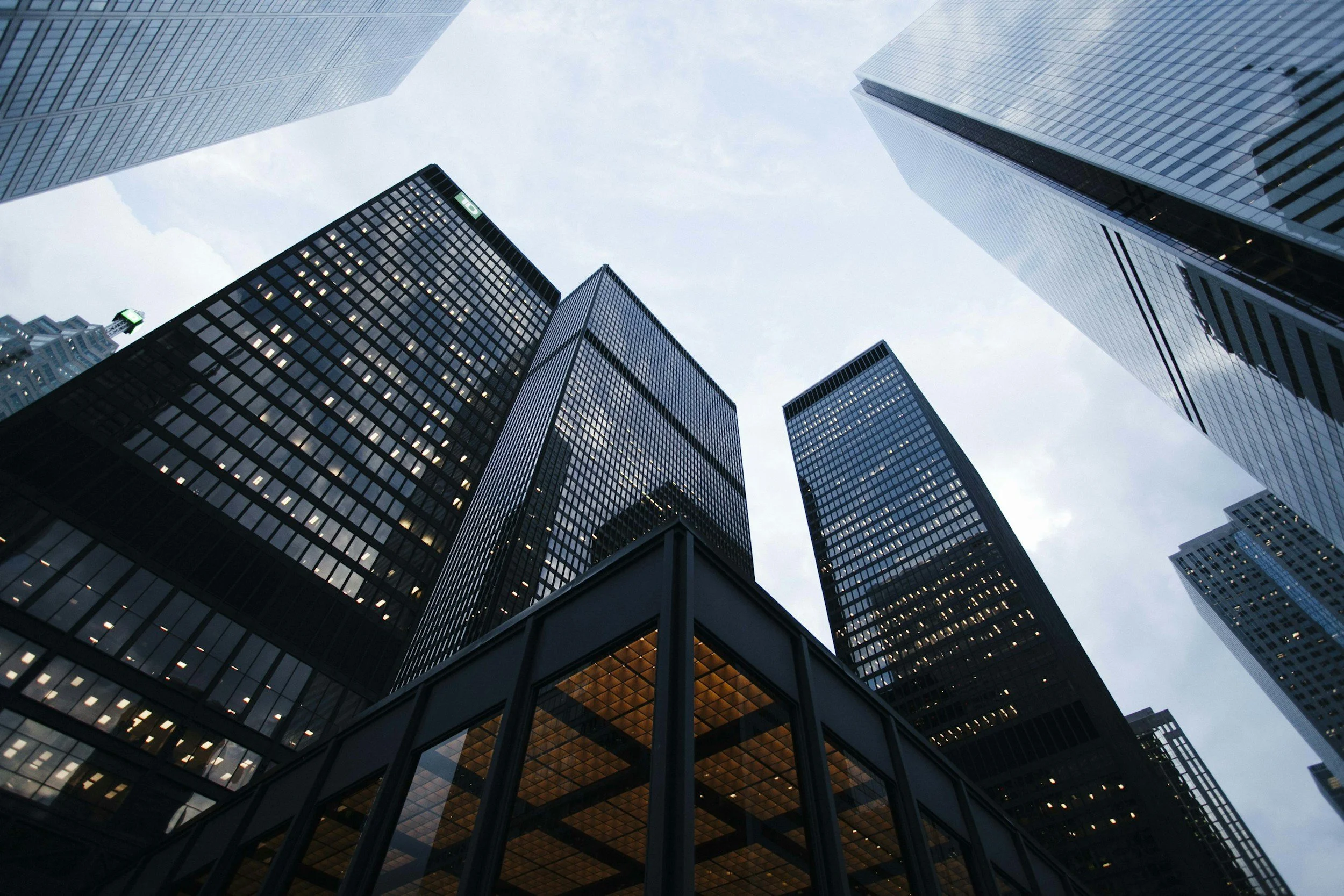 View of skyscrapers from ground level, looking up at the buildings with glass facades reflecting the cloudy sky.